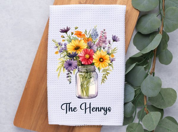 Mason jar filled with spring wild flowers and personalized with family name at the bottom on a white waffle weave hand towel.