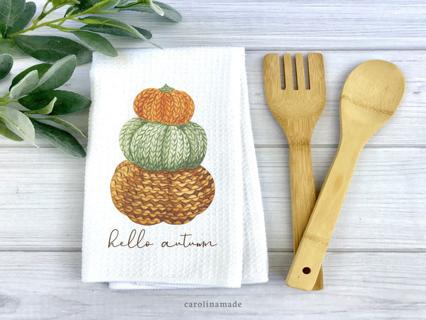 White waffle weave towel with stacked knitted pumpkins and the words hello autumn at the bottom.
