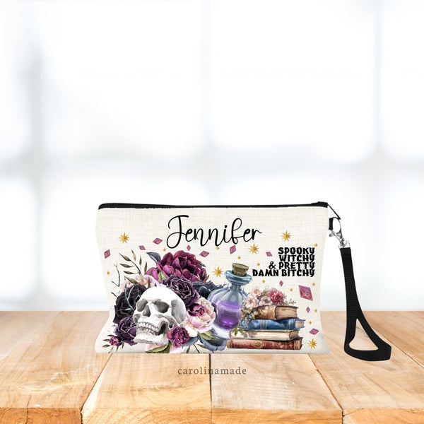This bag is personalized with a name at the top. And says Spooky Witchy & pretty damn Bitchy on the side. The bag features flowers behind a skull, with potion bottle and books.