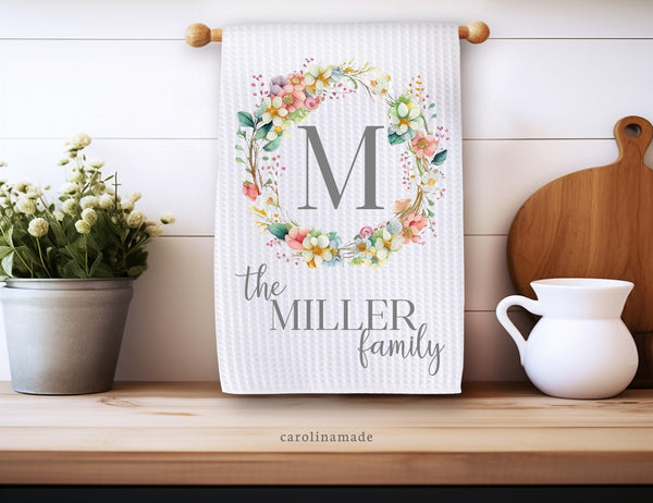 White waffle weave towel monogrammed with last name initial in the center of a spring flower wreath. The bottom is personalized with the family name.