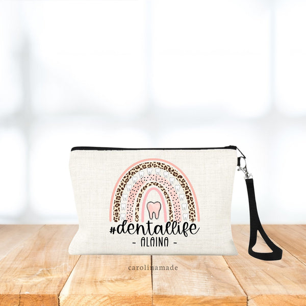 This linen bag with wristlet strap has large rainbow in the center with pink, leopard print and teeth. Under rainbow says dental life. And is personalized at the bottom with your name.