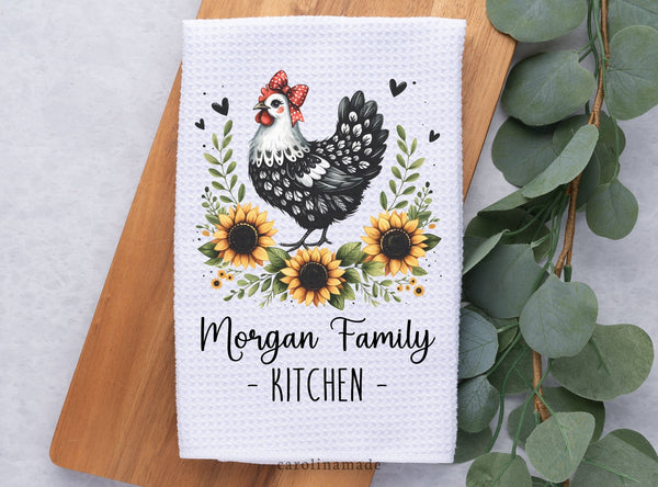 Black and white chicken surrounded by beautiful sunflowers and greenery on a white waffle weave towel. The bottom is personalized with Last Name Family Kitchen