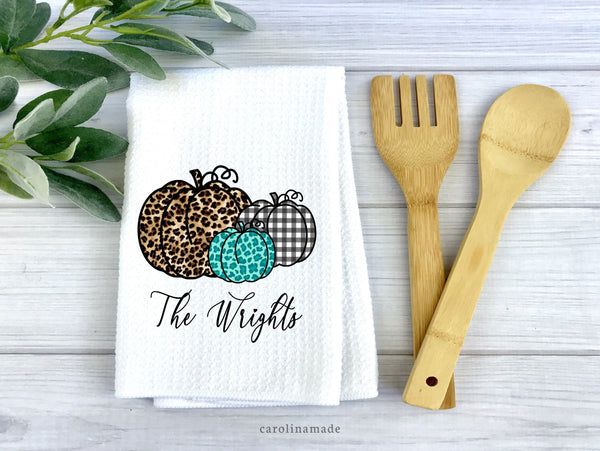 White waffle weave towel with three pumpkins - Large leopard print, teal leopard print, and black & white gingham plaid Pumpkin. Personalized with family name under them.