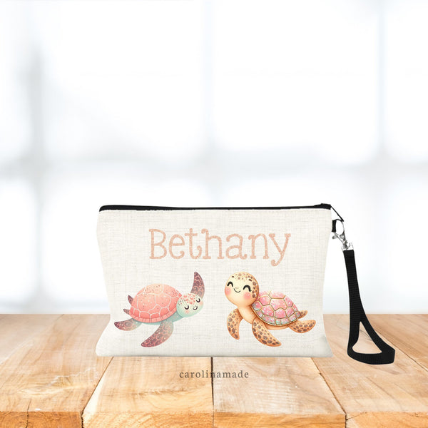 This linen wristlet is perfect for girls!It features a personalized name at the top in a printed rose gold glitter color. Under the name is two adorable sea turtles in various shakes of pink, teal, yellow.