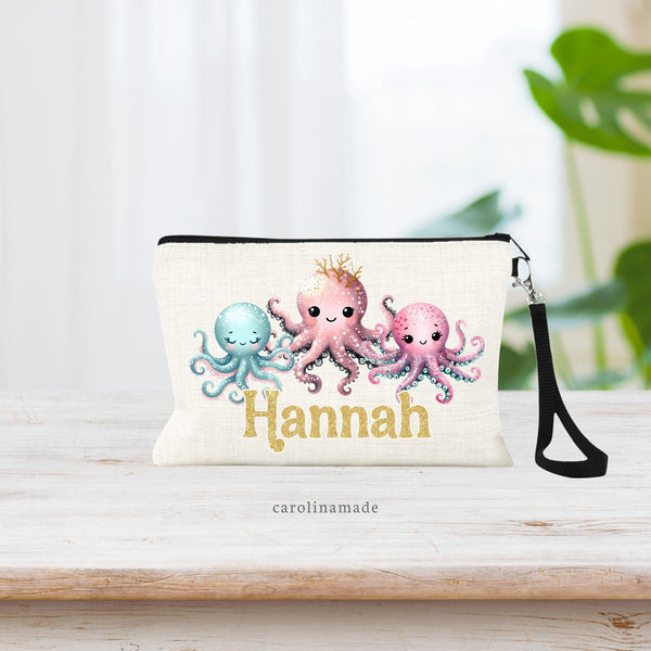 This zipper pouch shows a row of 3 octopuses. One teal, one a rose pink and one a brighter pink. The center one is larger & is wearing a coral crown. At the bottom your name is personalized in a printed gold glitter font.