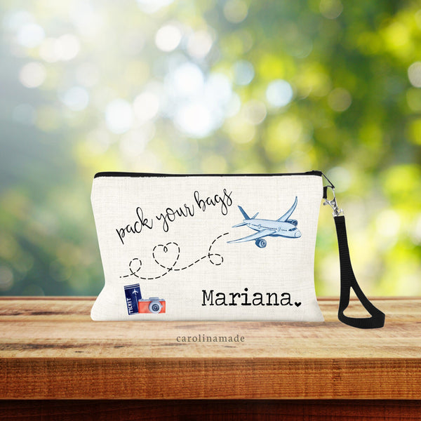 This natural linen bag with zipper & black wristlet strap features the text: pack your bags. With a dotted line leading to an airplane. In the bottom corner is clipart of a plane ticket & camera. The other side is personalized with a name & heart.