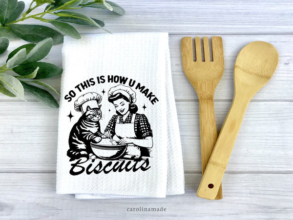 This white waffle weave towel says So this is how u make biscuits and shows a cat and woman with a baking bowl.