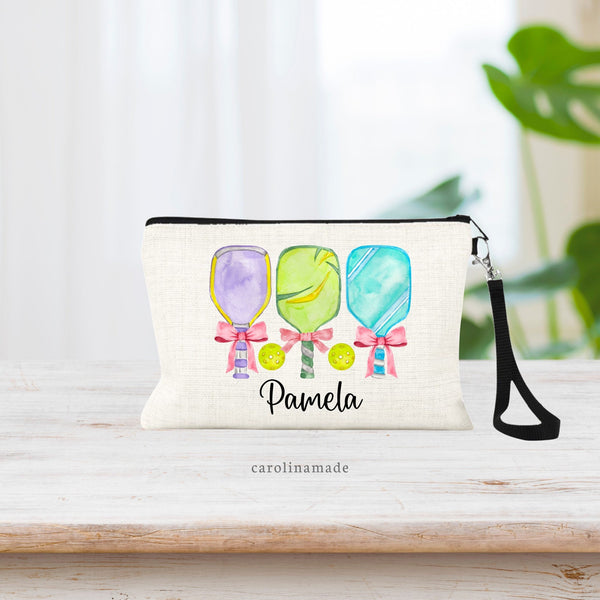 This linen zipper pouch features three beautiful watercolor pickleball paddles with pink coquette bows on the handle. The bottom is personalized with your name.