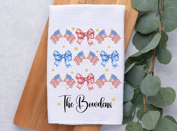 This white waffle weave towel features a watercolor red bow design pattern with a Red white & blue United States Flag. The bottom is personalized with your family name. And Gold stars surround the design