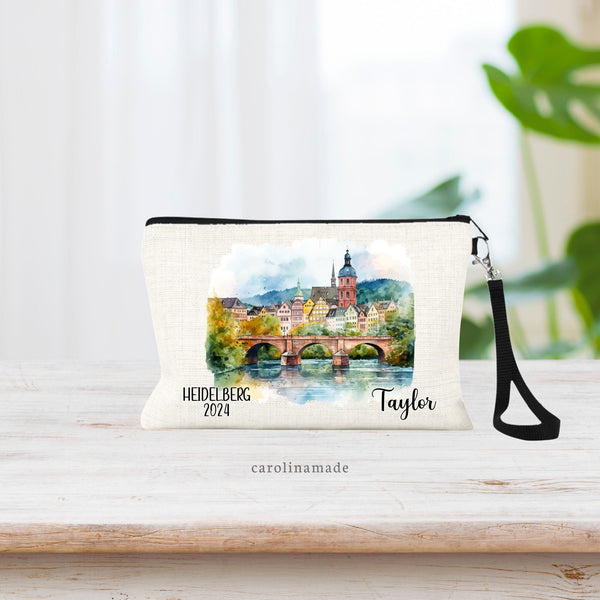 Watercolor Heidelberg Germany water, bridge, town scene in the center of the wristlet. The bottom says Heidelberg and the current year on the left. The right is personalized with your name.