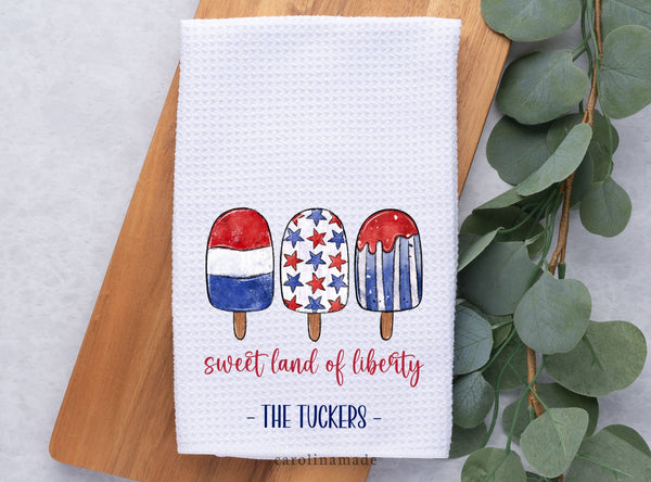 This white waffle weave towel features 3 red white and blue Popsicle with the script text sweet land of liberty under them. It is personalized at the bottom with your family name.
