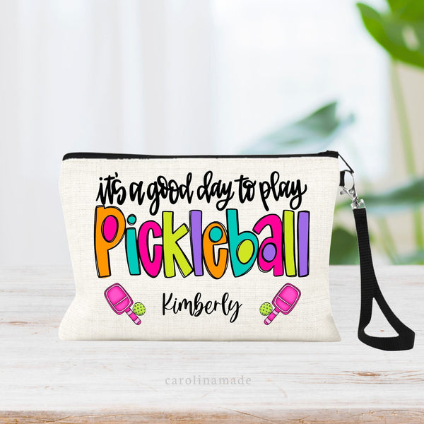 This colorful linen wristlet pouch is perfect for any pickleball player! Text says it's a good day to play pickleball with two paddles & balls at the bottom and your name between them.
