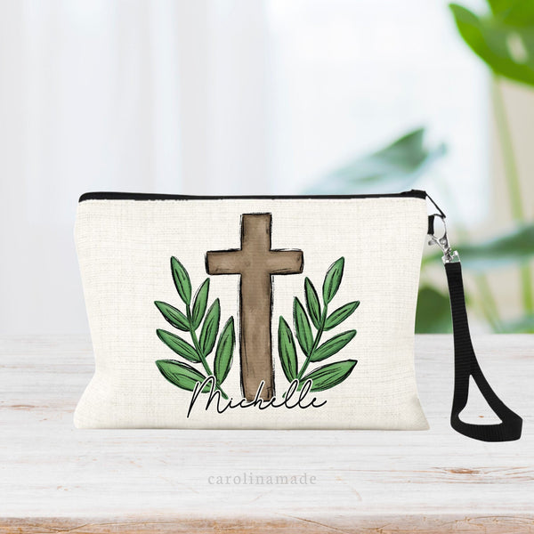 This zipper pouch features a large cross in the center with greenery on both sides. The bottom is personalized with your name.
