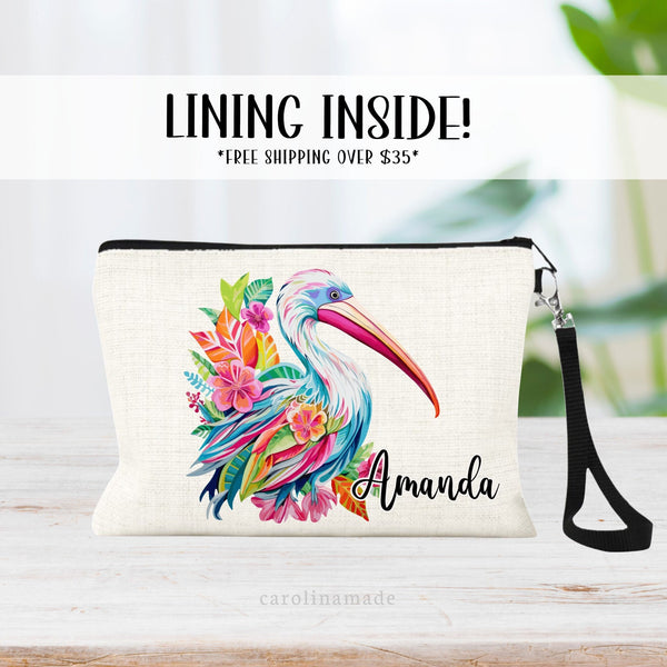 This linen zipper pouch features a large pelican with pink flowers, leaves and greenery in a preppy colorful design. It is personalized in the corner with a name.