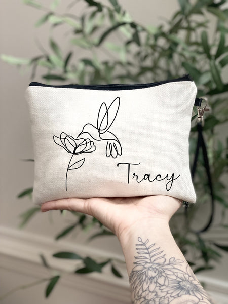 This linen zipper pouch features a minimalist line art design of a humming bird and flower. It is personalized next to the design with your name.
