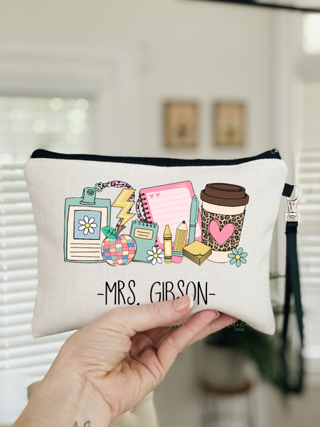 This linen wristlet shows teacher icons -notebook, badge, apple, pencil, crayon, pen, sticky notes, coffee and flowers. There is a name personalized at the bottom.