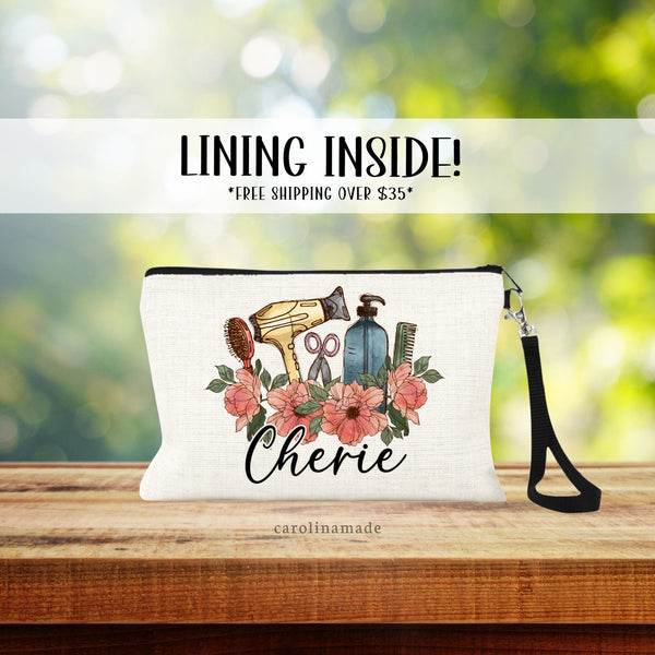 This linen pouch features hairstylist items surrounded by pink flowers. There is a brush, blow dryer, scissors, bottle, and comb. It is personalized at the bottom with a name.