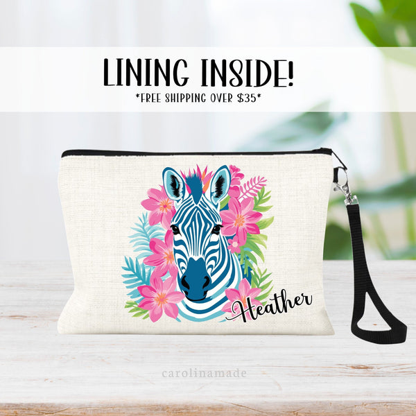 This linen zipper pouch features a pretty tropical floral, palm leaves and greenery design with a zebra in the center. It is personalized in the corner with your name.
