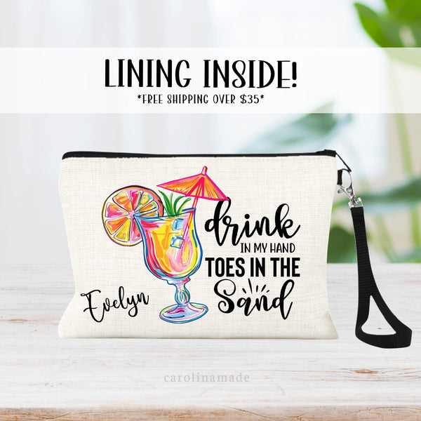 This linen zipper pouch features a preppy tropical cocktail on the left with the quote - drink in my hand toes in the sand. It is personalized with your name in the corner.