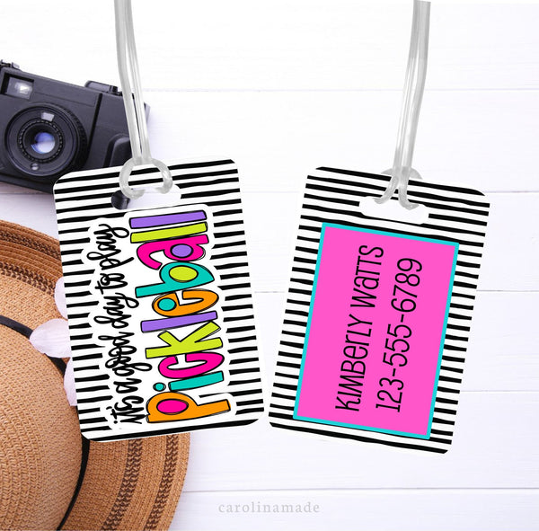 This bag tag features black and white stripes with a colorful design that says its a good day to play pickleball. The back is personalized your contact information.