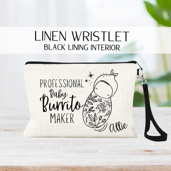 This linen wristlet features a black zipper, black lining and removable black strap. It shows a minimalist line art design of a baby wrapped in a swaddle and text says professional baby burrito maker. Personalized with your name in the corner.