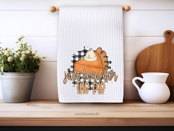 This white waffle weave towel features a black and white gingham design with a slice of pumpkin pie on top. The towel says just here for the pie