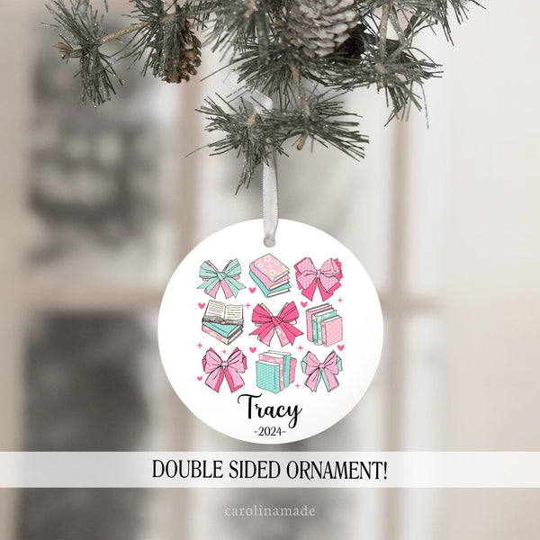 This ornament features a coquette bow design with bows in teal and pink pattern and stacks of books. It is personalized at the bottom with a name and current year. Perfect gift for book lovers!