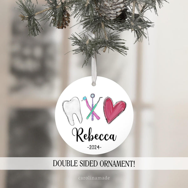 This ornament features a dental design with a tooth, dental tools and a heart. The bottom is personalized with a name and the current year.