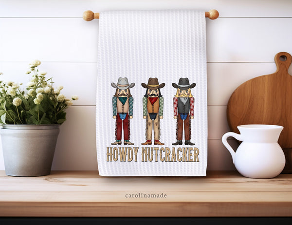 This white waffle weave towel features three cowboys in a row. The bottom says Howdy Nutcracker. The perfect Christmas towel decor.
