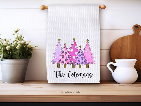 This white waffle weave towel features 4 pink and purple christmas trees in a row. It is personalized at the bottom with your family name.
