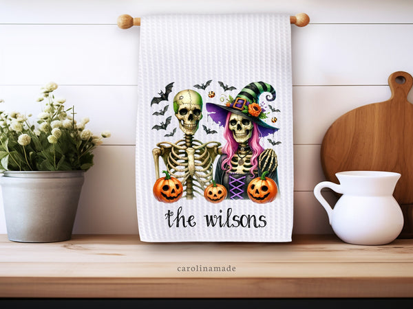 This white waffle weave towel features a skeleton couple dressed in halloween costumes with bats and pumpkins surrounding. It is personalized at the bottom with your family name.