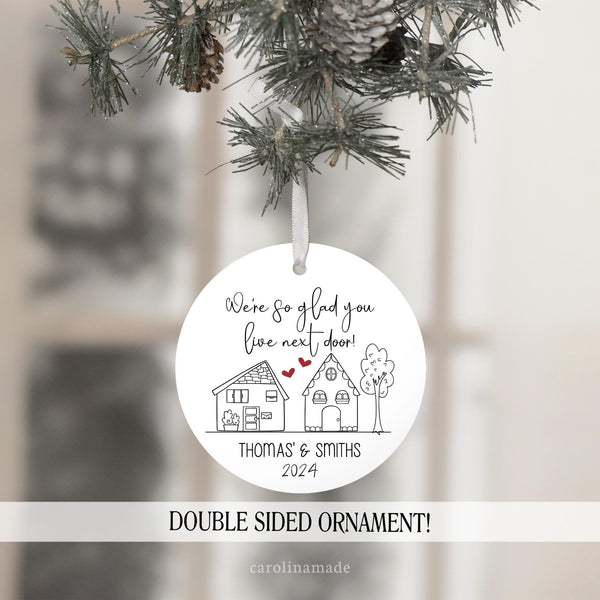 We are so glad you live next door Personalized Name Ornament. Featuring hand draw houses & tree with hearts between the houses. Bottom had family names & year