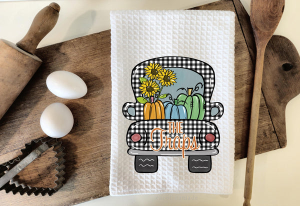 This white waffle weave towel features a black and white gingham truck filled with pumpkins and sunflowers. The truck is personalized with a name.