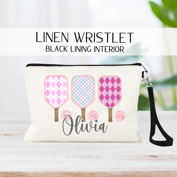 This linen wristlet features three pickleball paddles in a row with balls in a girly plaid and argyle pattern. It is personalized at the bottom with your name.