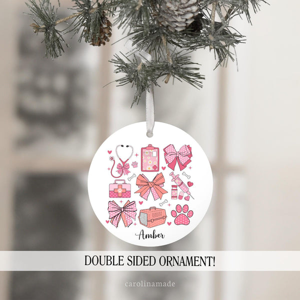 This pink bow veterinary ornament features design elements from a vet office. Clipboard, stethoscope, animal carrier, vet bag, paw print. It is personalized at the bottom with a name. Perfect gift for vet office!