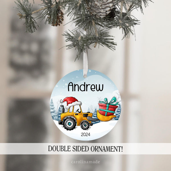 This fun ornament features a snowy background with a construction tractor with bucket carrying a Christmas present and wearing a Santa hat. It is personalized with your name at the top and the year at the bottom.