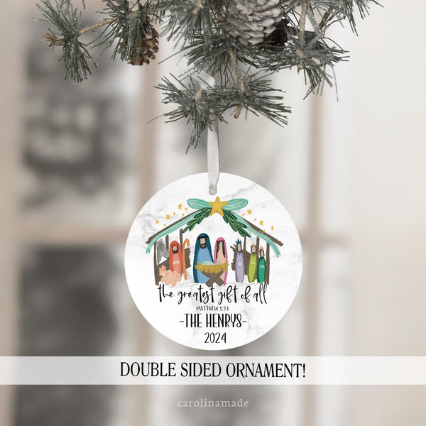 This ornament features a marble background with a manger and Jesus birth story. The text says the greatest gift of all Matthew 1 21. It is personalized with your family name and the year.
