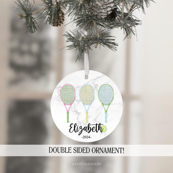 This christmas ornament features a marble background with three colorful tennis rackets and a ball. It is personalized at the bottom with your name and the year.