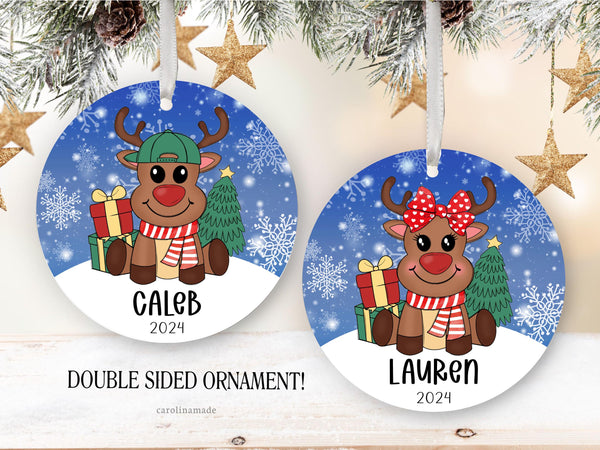 Christmas ornament for kids with snowy background and reindeer with presents and Christmas Tree. Choose deer with girl bow or ball cap. Personalized with name and year at the bottom.
