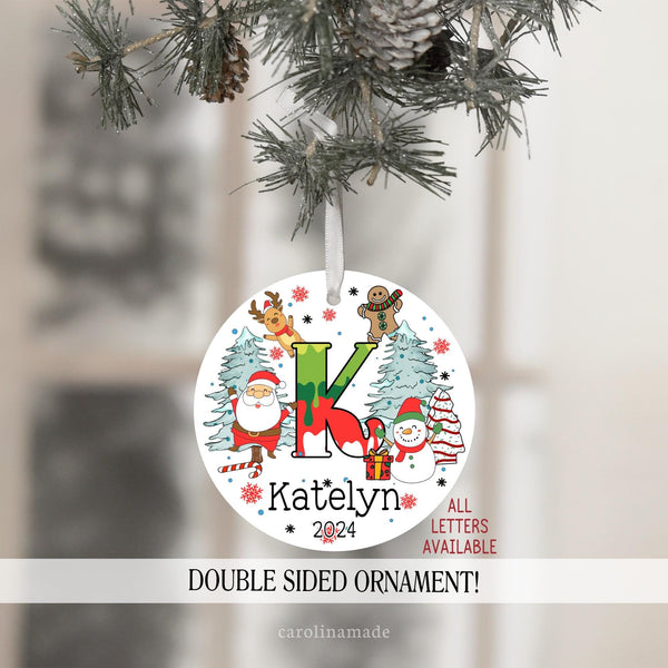 Kids Christmas Ornament with large initial in the center and Christmas art around it. Santa, candy canes, snowman, presents, gingerbread, snow and reindeer. Personalize with name and the year at the bottom.