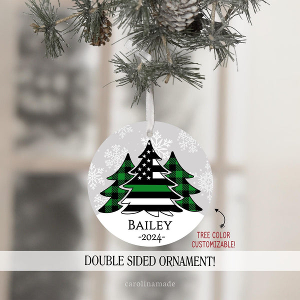 This ornament features gray snowy background with three Christmas trees in the center. Two with green plaid. And the center large tree is a flag with a thin green line for military. It is personalized at the bottom with your name and the year.