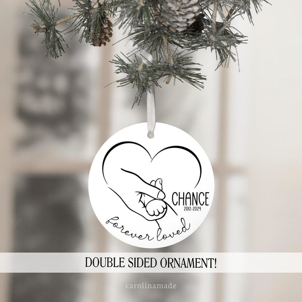 This ornament is black and white minimalist style. It features a cat paw in hand with a heart in the background. It says forever loved at the bottom. And is personalized with pets name and the year inside the heart.