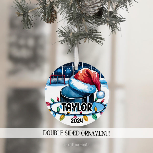 This Christmas ornament features a large hockey puck with a Santa hat in a hockey stadium with Christmas lights. It is personalized with your hockey players name and the year at the bottom.