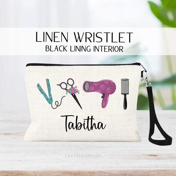 This linen pouch features hairstylist tools. There is a brush, blow dryer, scissors, and straightener. It is personalized at the bottom with a name.