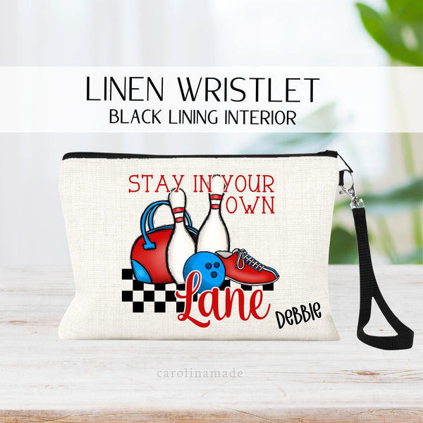 This linen zipper pouch features a red white and blue bowling design that says Stay in Your Own lane with ball, bowling pins, shoes and bag. It is personalized at the bottom with your name.