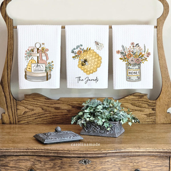 This listing shows a set of 3 waffle weave towels in a spring honey bee design. One towel has a tiered tray with spring decor, one is honey combs and flowers, and the 3rd is a set of spring wild flowers. Personalize the middle towel with honeycombs
