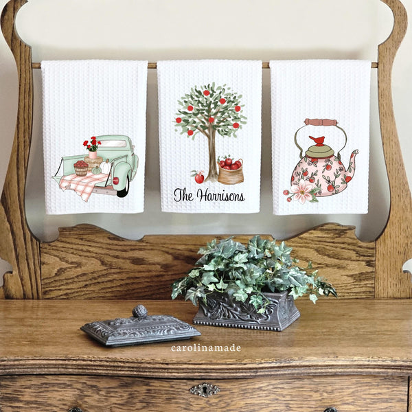 This set of three waffle wave towels features fall apple orchard designs. 1 with Truck, apples, pumpkins and flowers. Second with Apple Tree and basket of apples personalized with your family name. And third has apple tea kettle and flower.