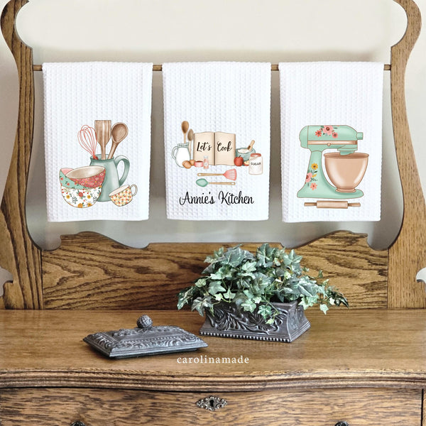 This three set of white waffle weave towels is perfect for anyone who loves to cook or bake! Kitchen utensils, bowls and cup on one towel, mixer on another, and the middle is personalized with your name and says lets cook and has cooking ingredients