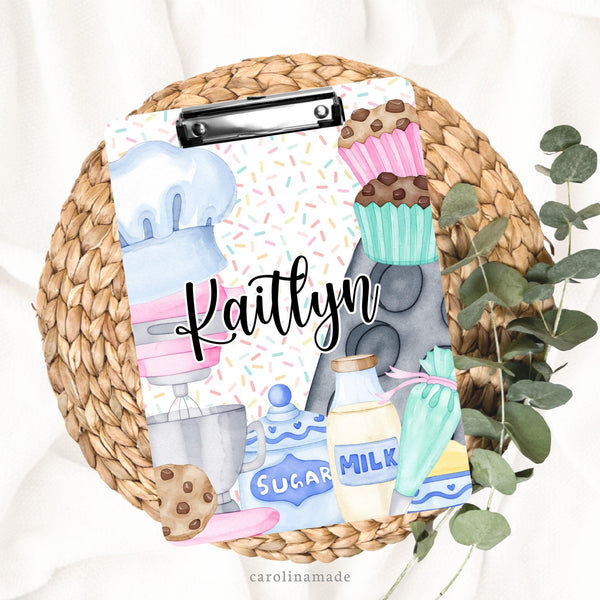 This double sided clipboard features a fun bakers design with a kitchen mixer, chefs hat, baking tin, cupcakes, sugar, milk and butter. The center is personalized with your name.
