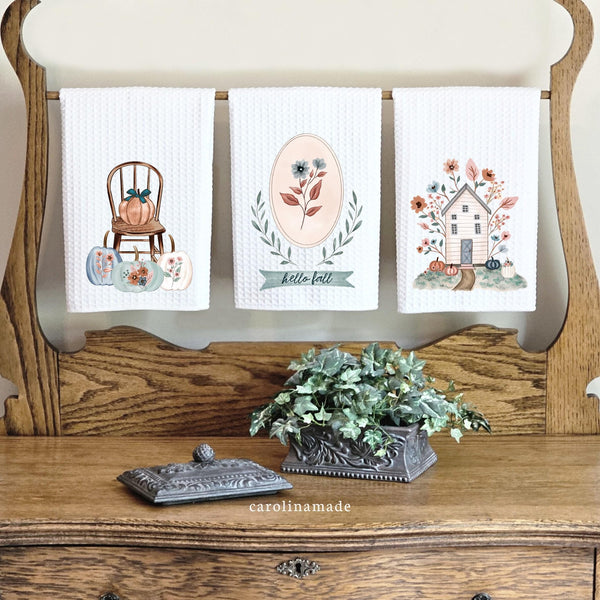 This set of three waffle weave towels features three different fall designs including pumpkins, fall floral and a house with flowers and pumpkins.